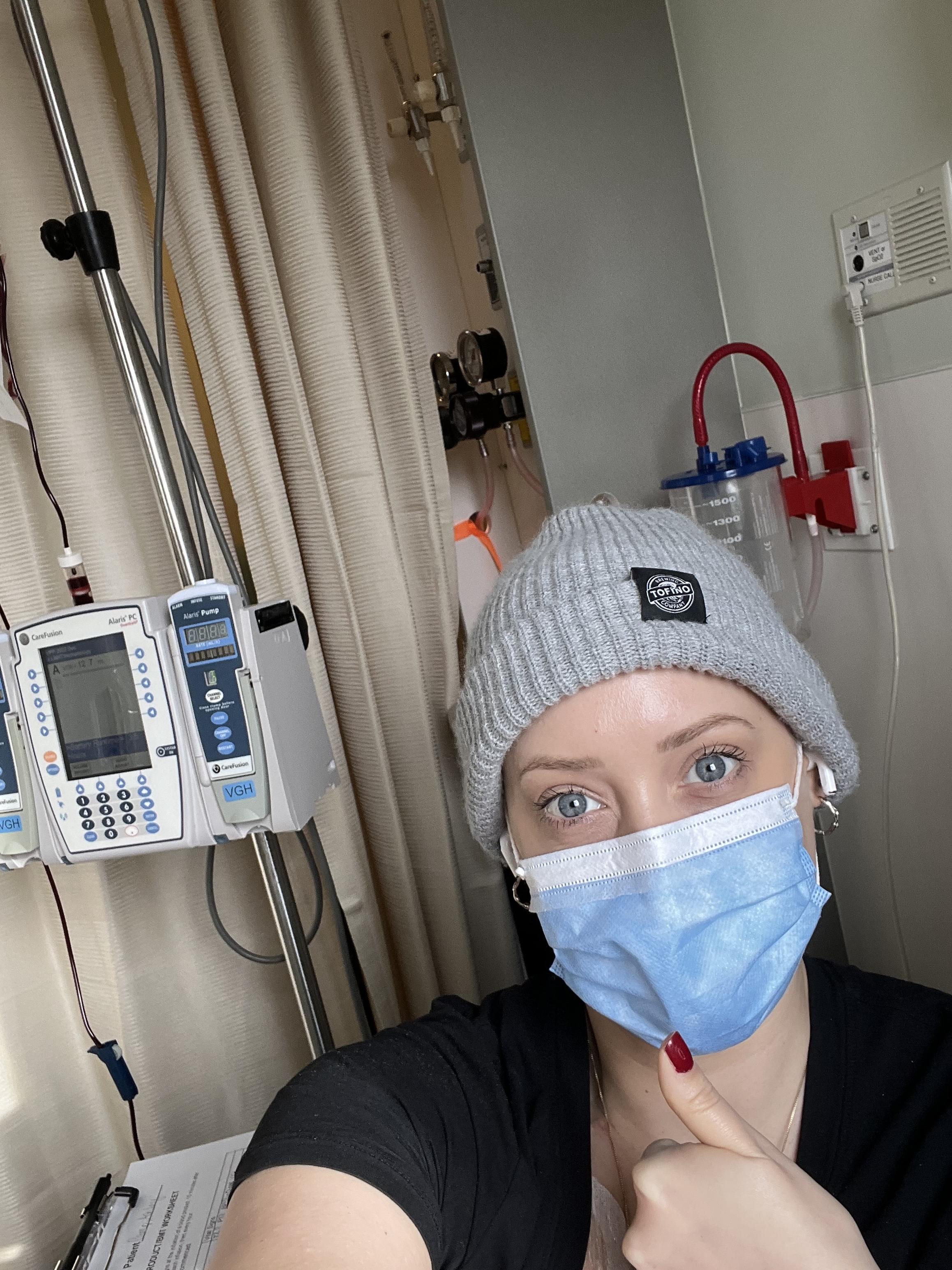 Ashley porte un masque dans une chambre d'hôpital, le pouce levé.
