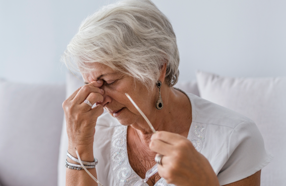 Une femme plus âgée aux cheveux gris enlève ses lunettes et se tient le nez en grimaçant.