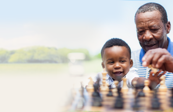 Un homme et son fils jouent aux échecs dehors dans un champ herbeux.