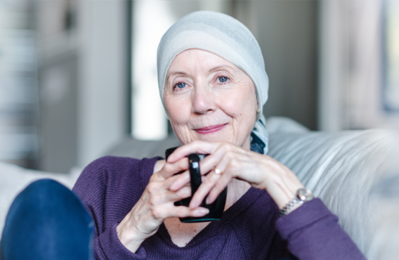 Femme souriante avec un tissu enveloppé sur sa tête, assise sur un canapé avec une tasse de café.