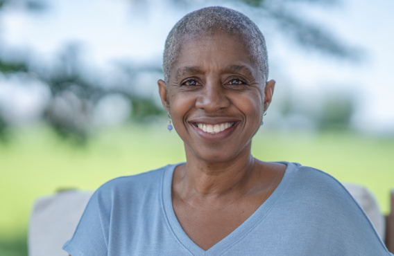 Femme souriante aux cheveux gris courts à l'extérieur devant un champ flou.