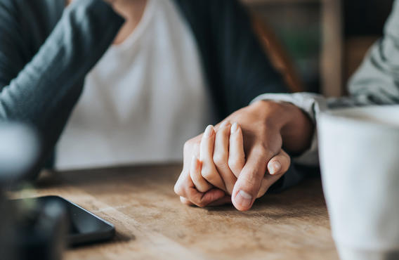 Two hands holding on a wooden table.