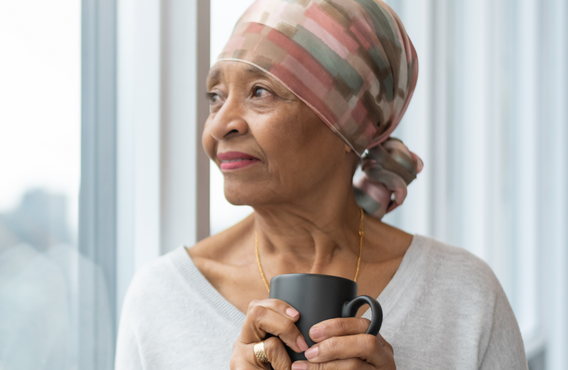 Une personne portant un foulard à motifs et tenant une tasse se tient près d'une grande fenêtre.  Une douce lumière naturelle éclaire la scène, avec la silhouette floue de la ville en arrière-plan.