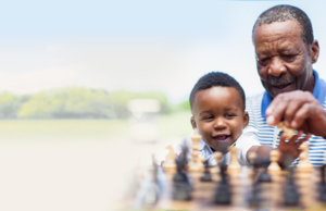 Un homme et son fils jouent aux échecs dehors dans un champ herbeux.