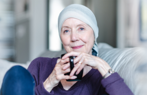 Femme souriante avec un tissu enveloppé sur sa tête, assise sur un canapé avec une tasse de café.