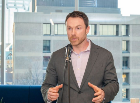 Paul debout sur un podium, parlant dans un microphone