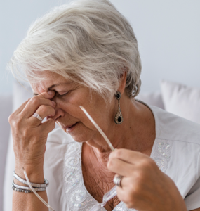 Une femme plus âgée aux cheveux gris enlève ses lunettes et se tient le nez en grimaçant.