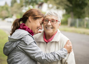 Une femme d’âge moyen serrant dans ses bras une femme plus âgée. Tous deux sont dehors et sourient.