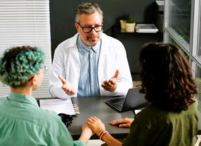 Un médecin assis avec deux patients discutant de quelque chose.