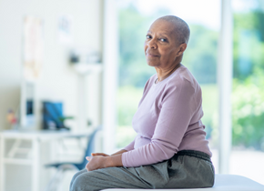 A woman sits on a table in a doctor's office. She is looking at the camera.