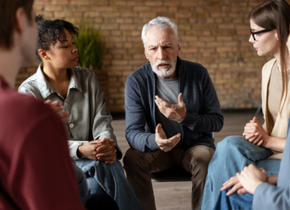 iverse group of individuals engaged in listening to a senior man sharing insights during a supportive group therapy session