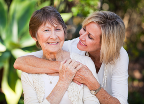 A woman embraces an older woman. They are outside. The older woman is looking at the camera.