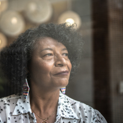 An older Black woman with colourful earrings looks out a window.