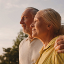 A man and a woman are outside in the golden hour. They are looking off in the distance.