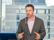 Paul debout sur un podium, parlant dans un microphone