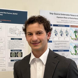A man in a suit stands in front of a medical poster.