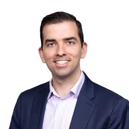 A man with short dark hair looks at the camera. He is wearing a suit.