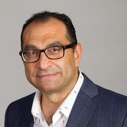 A man with short hair and glasses looks at the camera