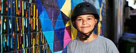 A boy named Justin with a helmet on standing beside a colourful wall.